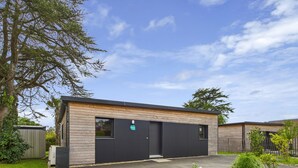 A modern building with a wooden facade and a black door, surrounded by greenery and a clear sky. - New house with terrace and garden for 6 (Fouesnant)