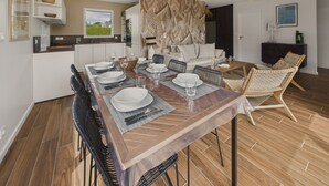 A modern dining area with a wooden table set for four, surrounded by wicker chairs. - New house with terrace and garden for 6 (Fouesnant)