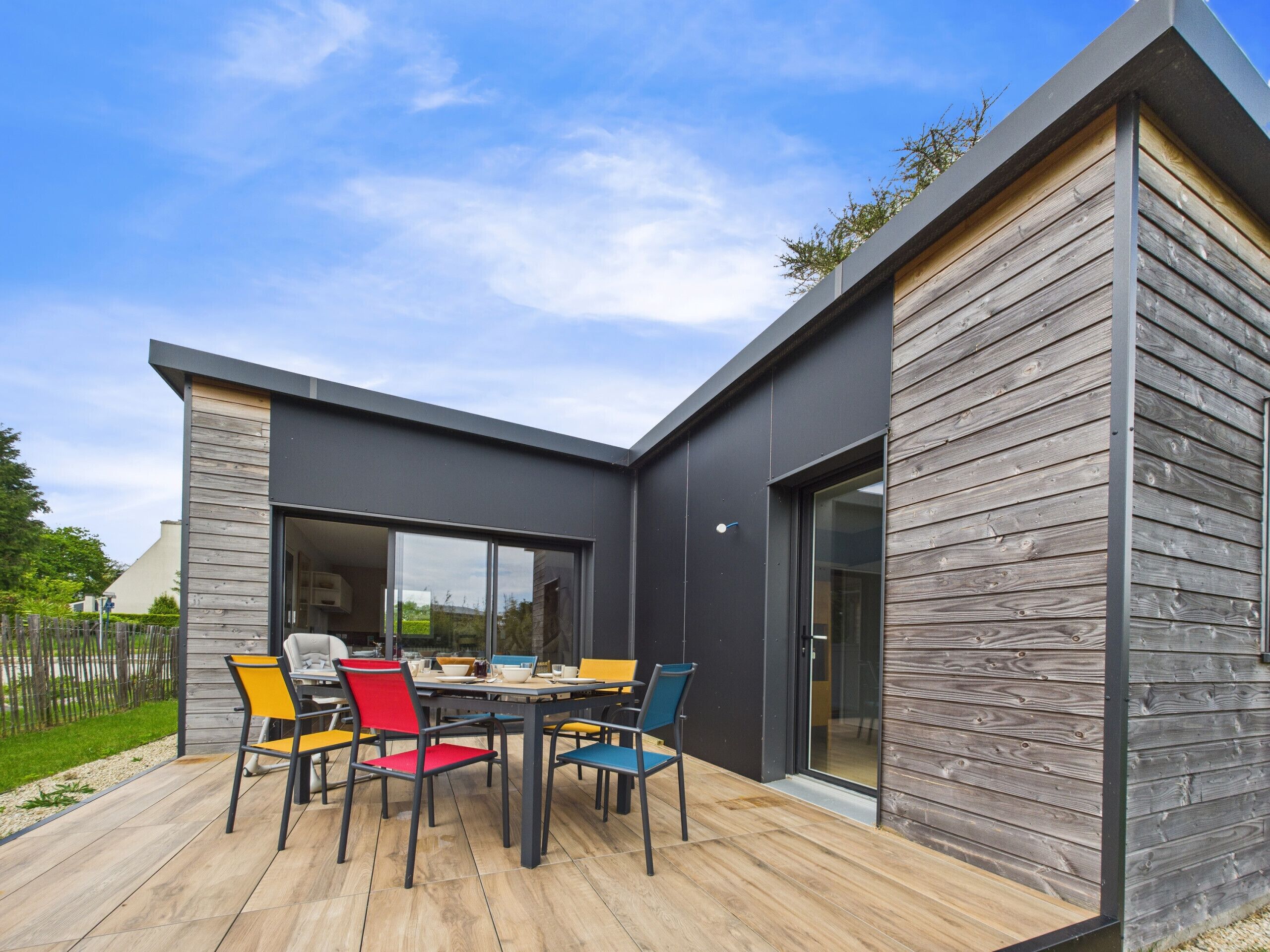 Un área de comedor al aire libre y moderna con una terraza de madera, una mesa y sillas coloridas.