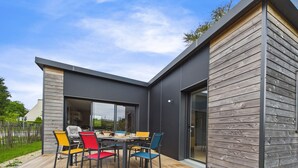 A modern outdoor dining area with a wooden deck, a table, and colorful chairs. - New house with terrace and garden for 6 (Fouesnant)