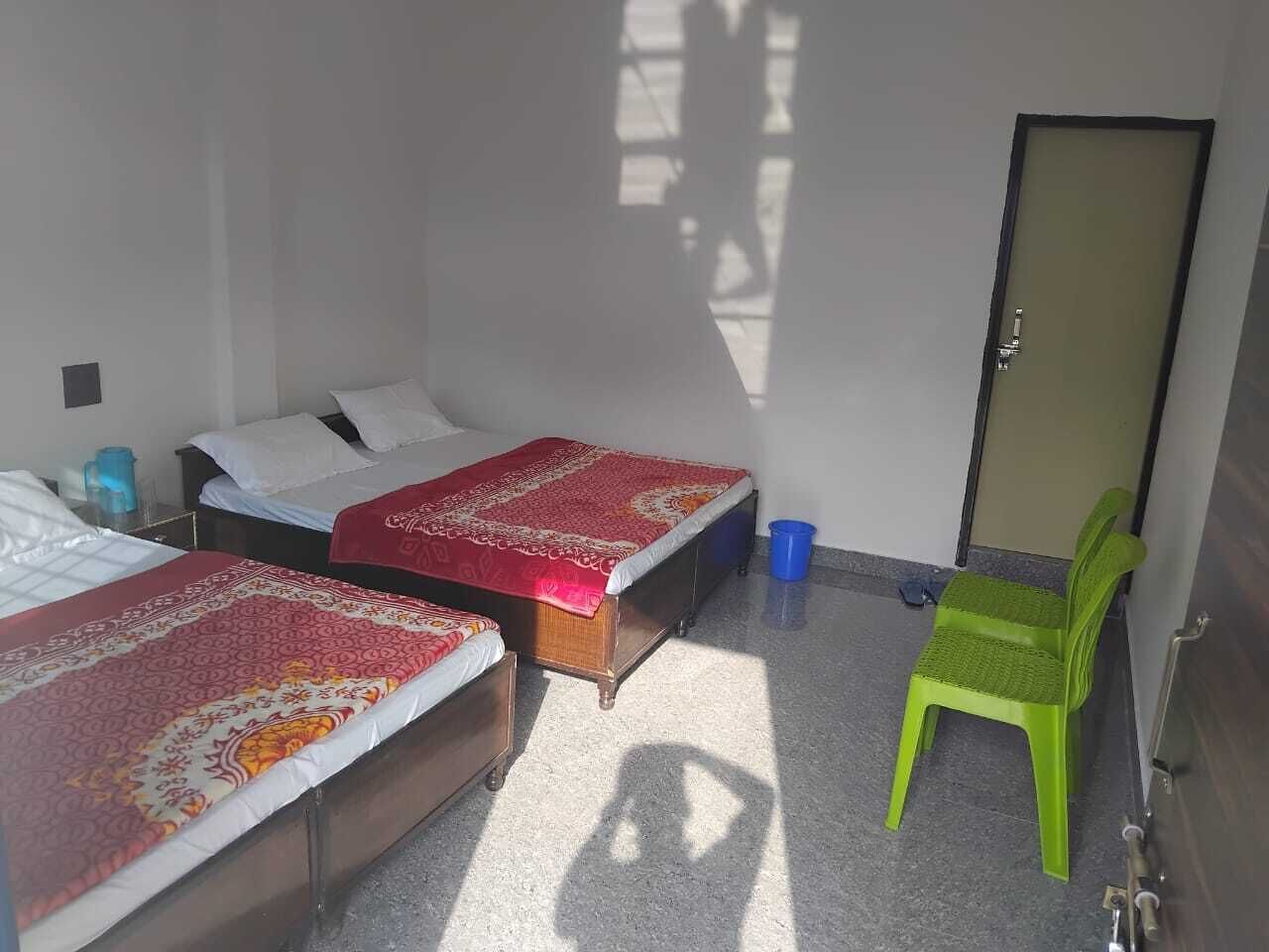 Une petite pièce avec deux lits simples, une chaise en plastique verte et une porte.