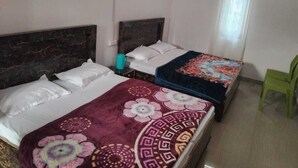 Ein Zimmer mit zwei Betten, jeweils mit Kopfteil, einem Fenster mit Vorhang und einem grünen Sessel.