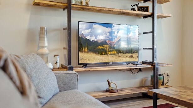 Uma sala de estar moderna com TV fixada na parede, estantes de madeira e um sofá aconchegante.