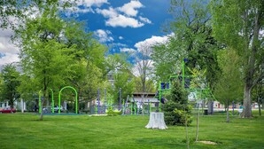 Um parque com equipamentos de recreação, árvores e um edifício ao fundo.