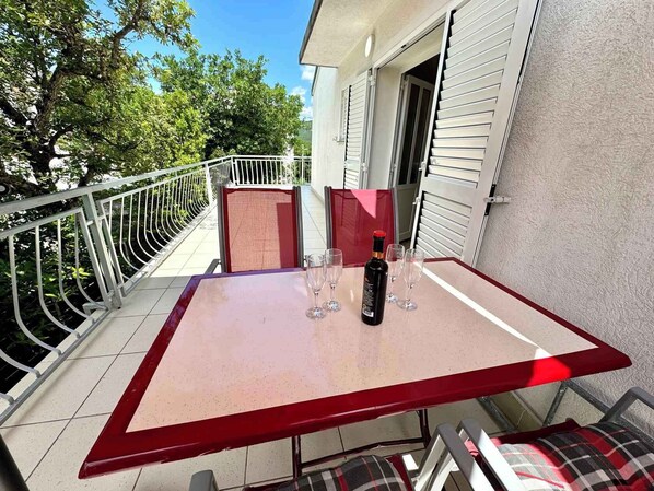 Una mesa con una botella de vino y copas en un balcón con baranda de metal.