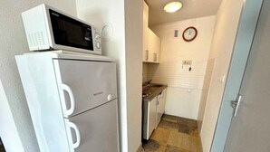 Cocina compacta con refrigerador blanco, microondas encima, pileta y un reloj en la pared.
