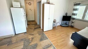 Habitación compacta con kitchenette, armario, pequeña mesa con tetera, televisor y ventana con cortinas.