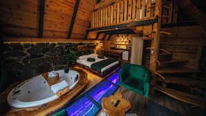 L’intérieur d’un chalet confortable, avec des murs en pierre, un lit en bois, une baignoire et un fauteuil vert.
