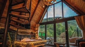 Une pièce chaleureuse avec une cheminée en pierre, un plafond en bois et une grande fenêtre donnant sur l’extérieur.