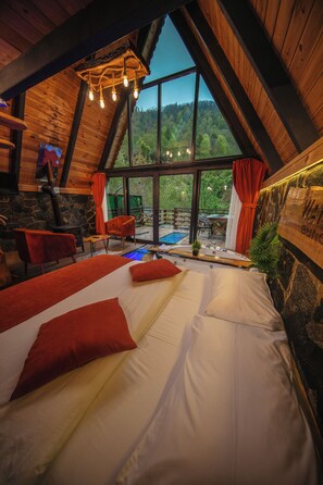 Une chambre confortable avec un grand lit, un plafond en bois et une vue sur une zone boisée.