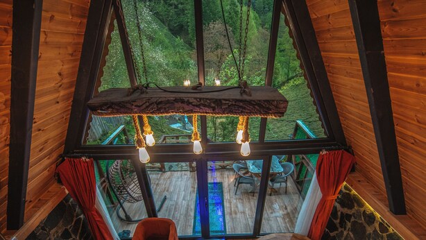 Un intérieur de chalet chaleureux, avec un décor en bois, une cheminée en pierre, un bain à remous et une vue sur la forêt.