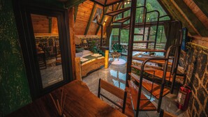 Un intérieur rustique en bois, avec un espace repas en mezzanine, des murs en pierre et une vue sur la forêt.