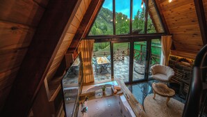 Un intérieur en bois avec une grande fenêtre en verre, une baignoire, une chaise et une cheminée en pierre.
