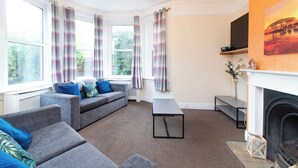 A living room with a fireplace, a sofa set, a coffee table, and a TV mounted on the wall. - Thornbury Guest House Room 2 (Southampton)