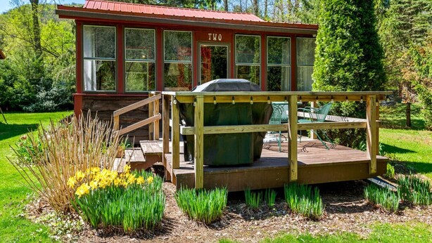 Een klein houten huisje met een rood dak en het nummer '20' op de gevel, omringd door een tuin met gele bloemen en groene planten.