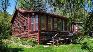 A rustic log cabin with a red exterior, large windows, and a wooden staircase leading to the entrance. - "Rocky Bottom" Cabin • Creekside • Fire Pit • BBQ • Fishing (Phoenicia)