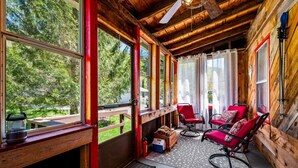 A cozy cabin with wooden walls and a wooden ceiling. There are two red chairs with cushions, a bench, and a small table. The cabin has large windows with curtains, and a door is visible. - "Rocky Bottom" Cabin • Creekside • Fire Pit • BBQ • Fishing (Phoenicia)