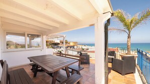 A covered outdoor patio with a wooden table and benches, overlooking a beach and the sea. - Apartment Breathtaking View 200 meters from the Sea! (Alcamo)