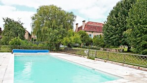 Una piscina rectangular con una cubierta azul, rodeada por una valla blanca y vegetación.