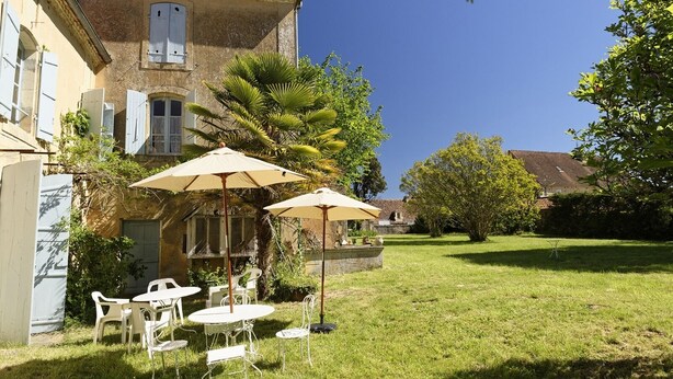 Un patio con un edificio, mobiliario exterior y una palmera.