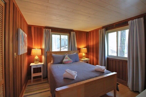 A wooden-paneled bedroom with a bed, two bedside lamps, and a window with curtains.