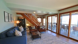 A spacious living area with a blue sofa, two armchairs, a coffee table, and a staircase leading to a balcony. - Bald Mountain Lake Retreat (Lake Lure)