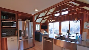 A modern kitchen with stainless steel appliances, wooden beams, and a large window overlooking a deck. - Bald Mountain Lake Retreat (Lake Lure)
