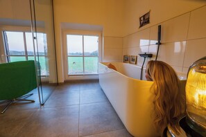 Un baño con bañera, un ventanal y vista a un cuerpo de agua.