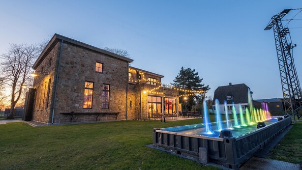A stone building with a balcony and a fountain with colorful lights. - E-Loft Altes Wasserwerk Tecklenburg (Tecklenburg)
