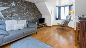 A modern living room with a grey leather sofa, a wooden coffee table, and a star decoration on the brick wall. - Creel Cottage 4 - Stunning Beach Front Access & Views - Free Parking - Garden (Arbroath)