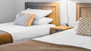A hotel room with two beds, each with white linens and a wooden headboard. There is a wooden nightstand between the beds with a lamp and a power outlet. - Creel Cottage 4 - Stunning Beach Front Access & Views - Free Parking - Garden (Arbroath)