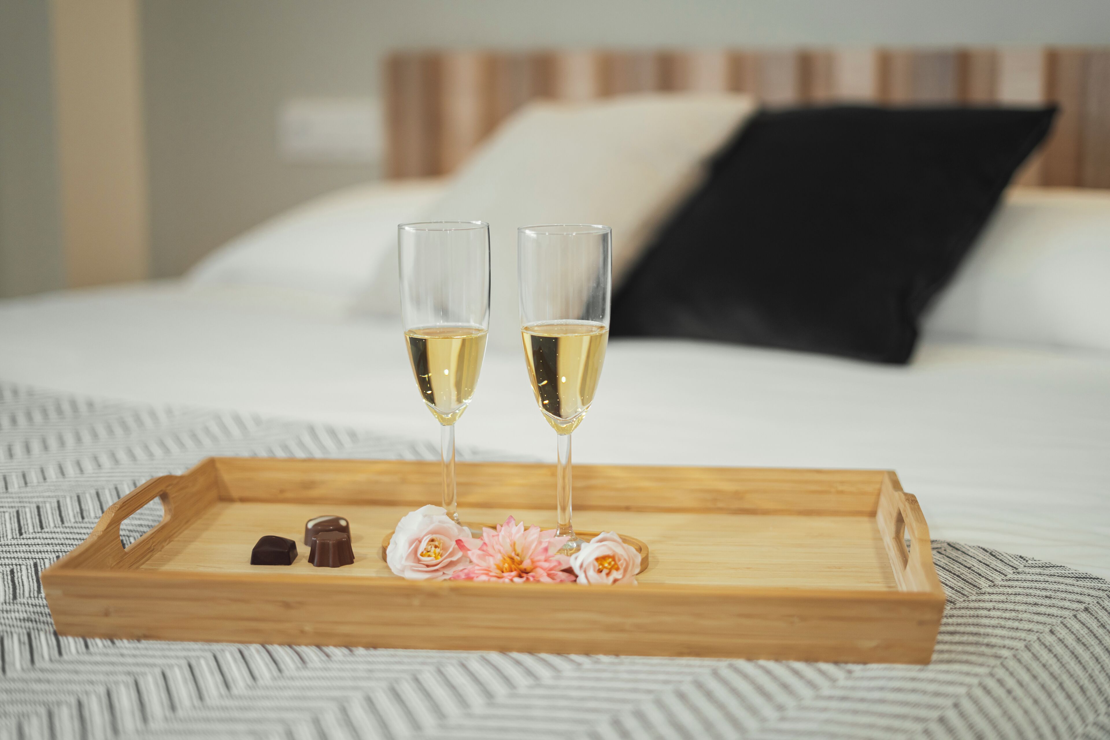 Un plateau en bois avec deux coupes de champagne, des chocolats et des fleurs disposés dessus.