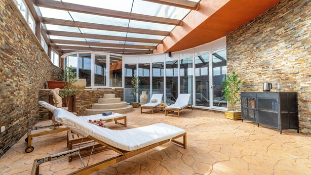A sunlit patio with lounge chairs, a stone floor, and a glass-enclosed area with a view.