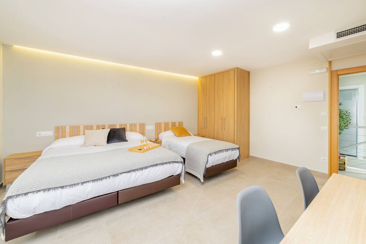 A modern hotel room with two beds, a wooden wardrobe, a desk, and a chair.