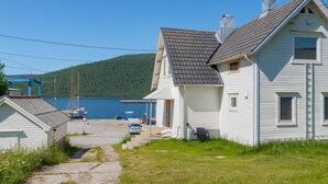 A coastal house with a dock, a small boat, and a view of the water and hills.
