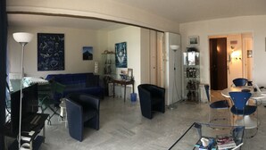 A living room with a sofa, a dining table with chairs, a laptop on a table, and various decorative items on the walls. - Seafront apartment close to beaches and Esterel: absolute calm (Saint-Raphaël)