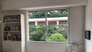 A bedroom with a large window, a bookshelf, a radiator, and a bedside table with a lamp. - Seafront apartment close to beaches and Esterel: absolute calm (Saint-Raphaël)