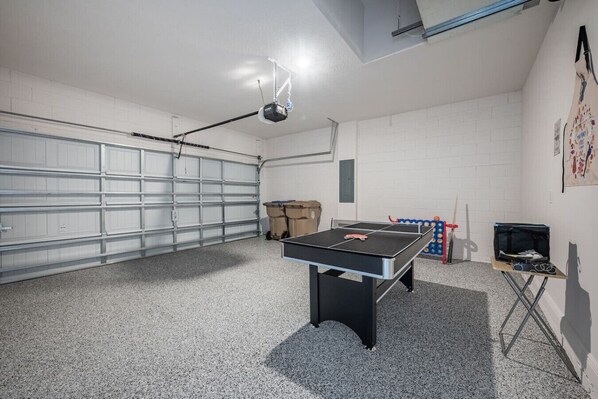 Une pièce équipée d’une table de ping-pong, d’un projecteur et d’une porte de garage.