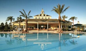 Un grand hôtel doté d’une piscine, de palmiers et d’un patio couvert.