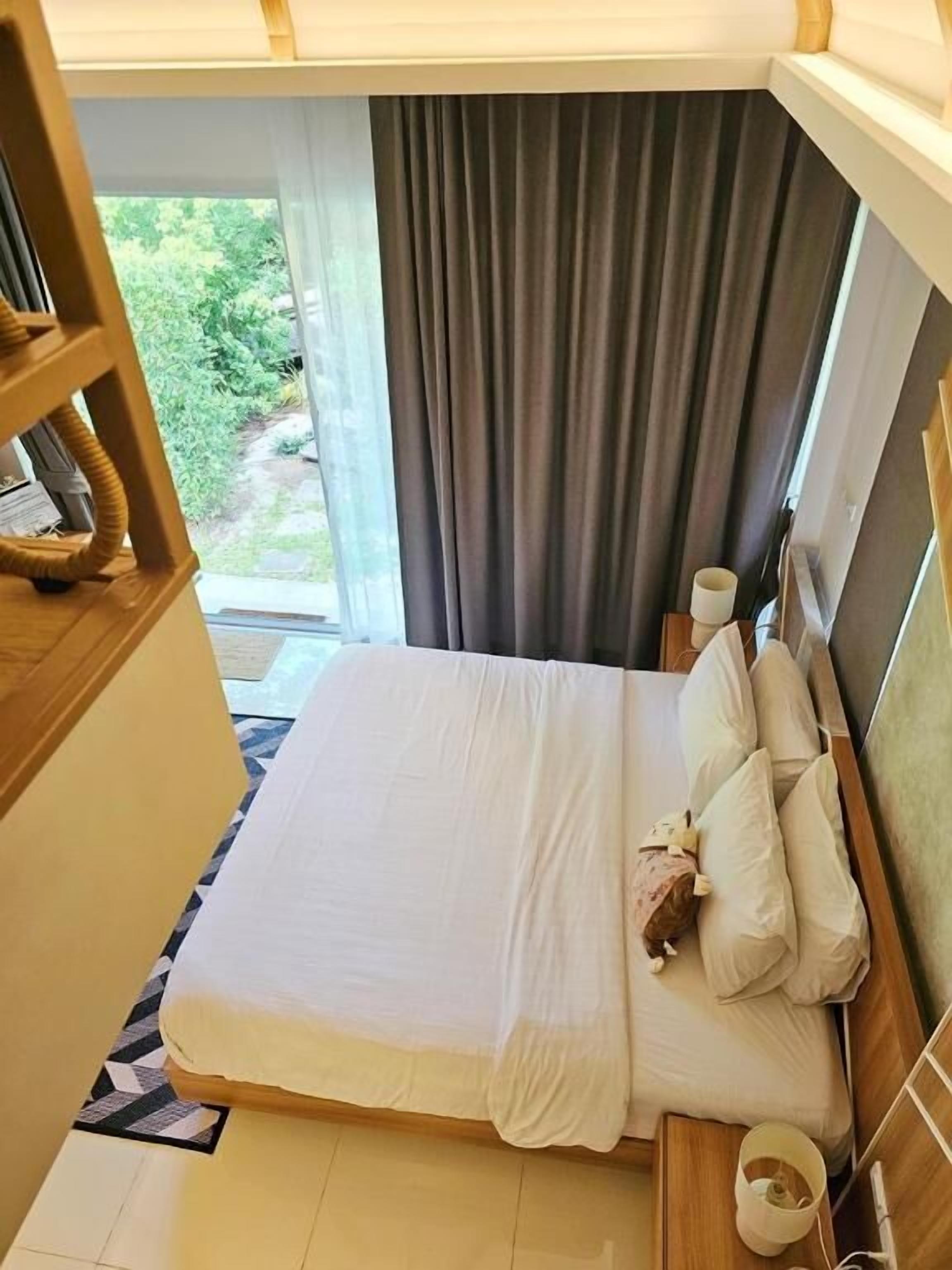 Hotellihuone, jossa on sänky, tyynyjä, yöpöytä ja näkymä vihreälle alueelle.