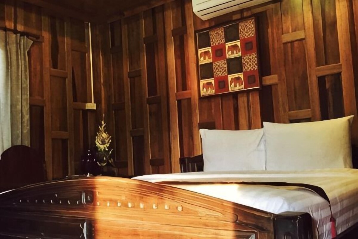 A wooden-paneled room with a bed, a chair, and a wall-mounted shelf.