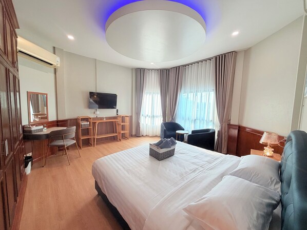 Habitación de hotel con cama, escritorio, silla, televisor y ventana con cortinas.