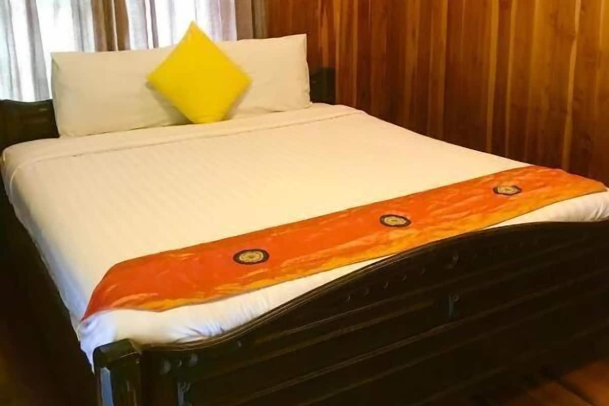 A wooden-paneled room with a bed, white bedding, and a yellow pillow.