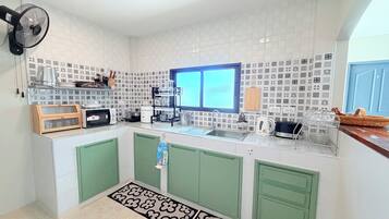 A kitchen with white tiled backsplash, green cabinets, a window, and a fan.