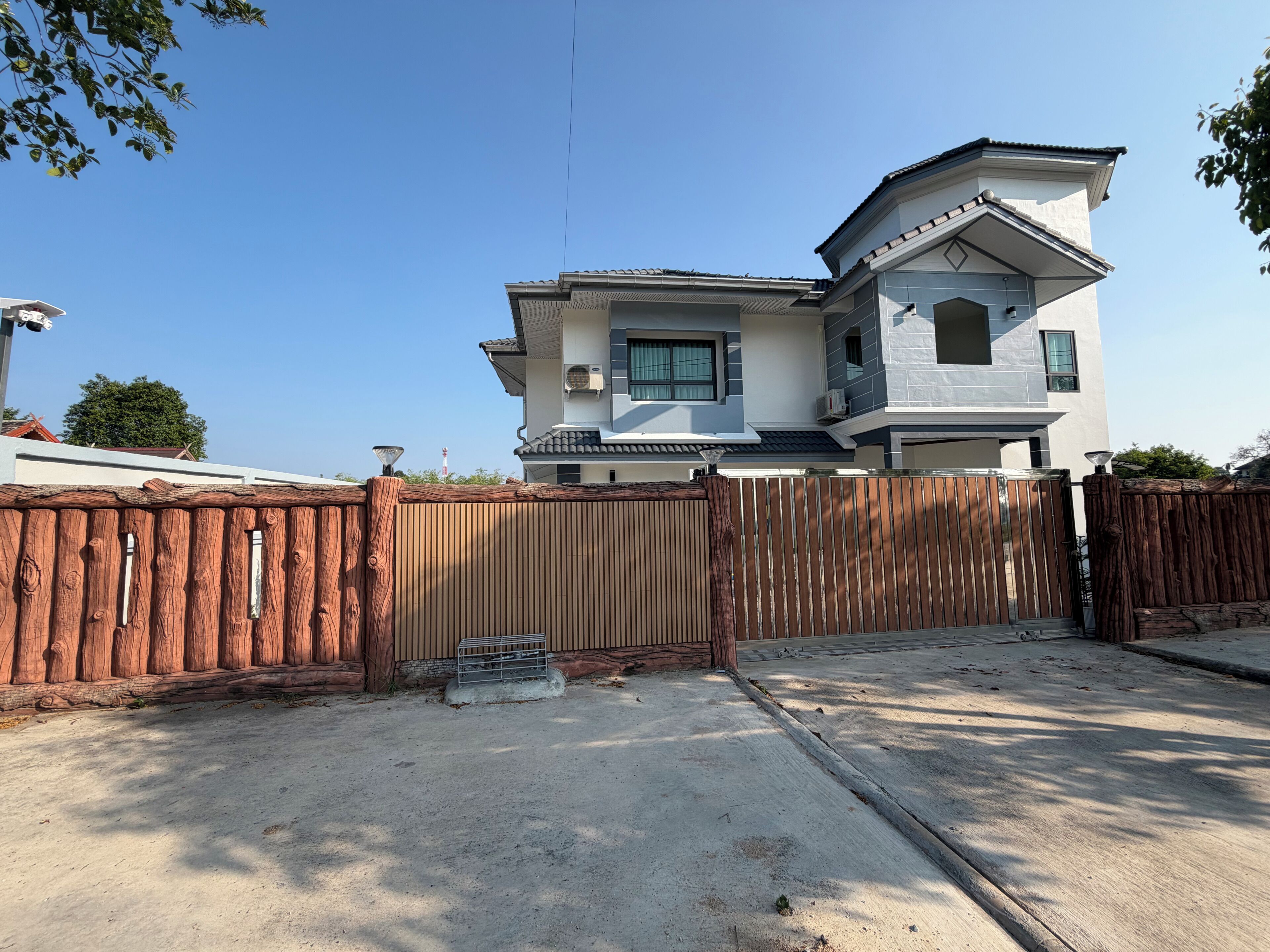 A two-story house with a gated driveway, a concrete patio, and a wooden fence.