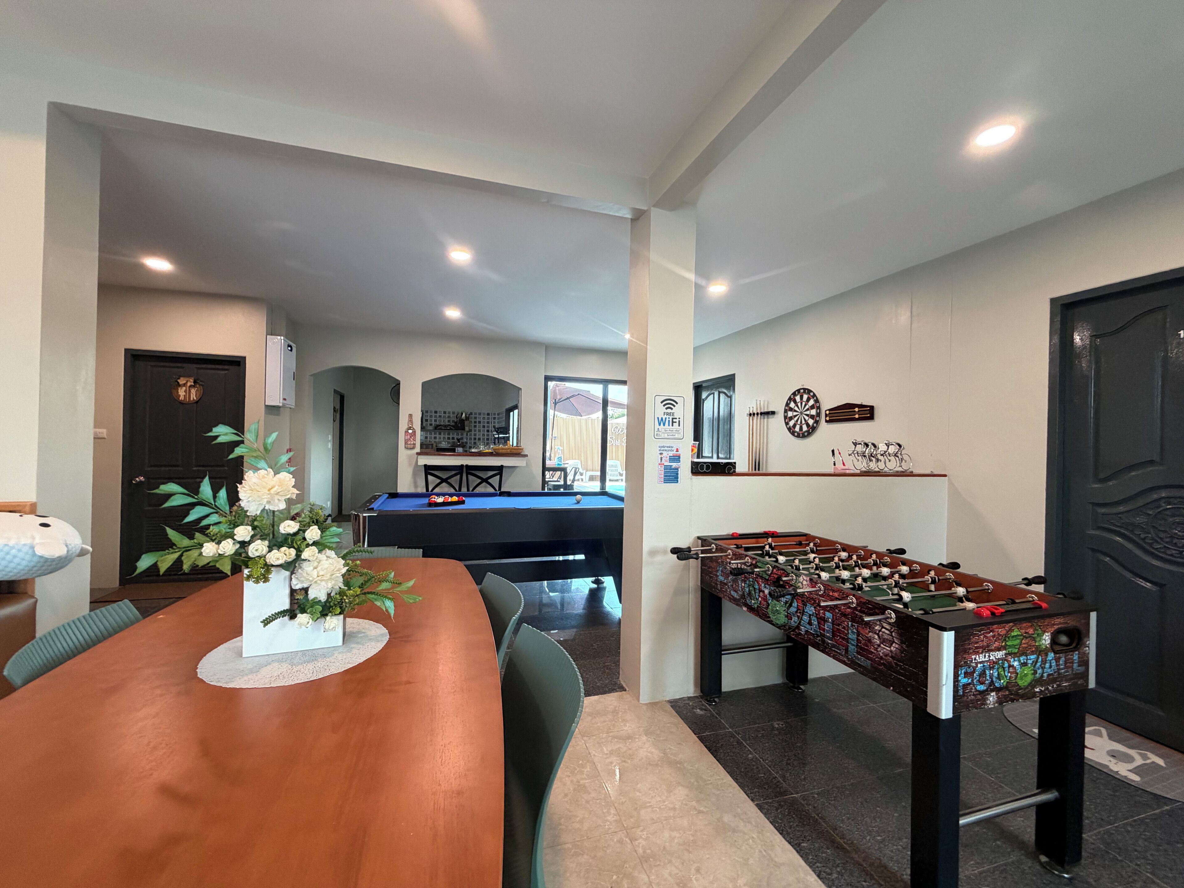 A dining area with a pool table, a foosball table, and a kitchen in the background.