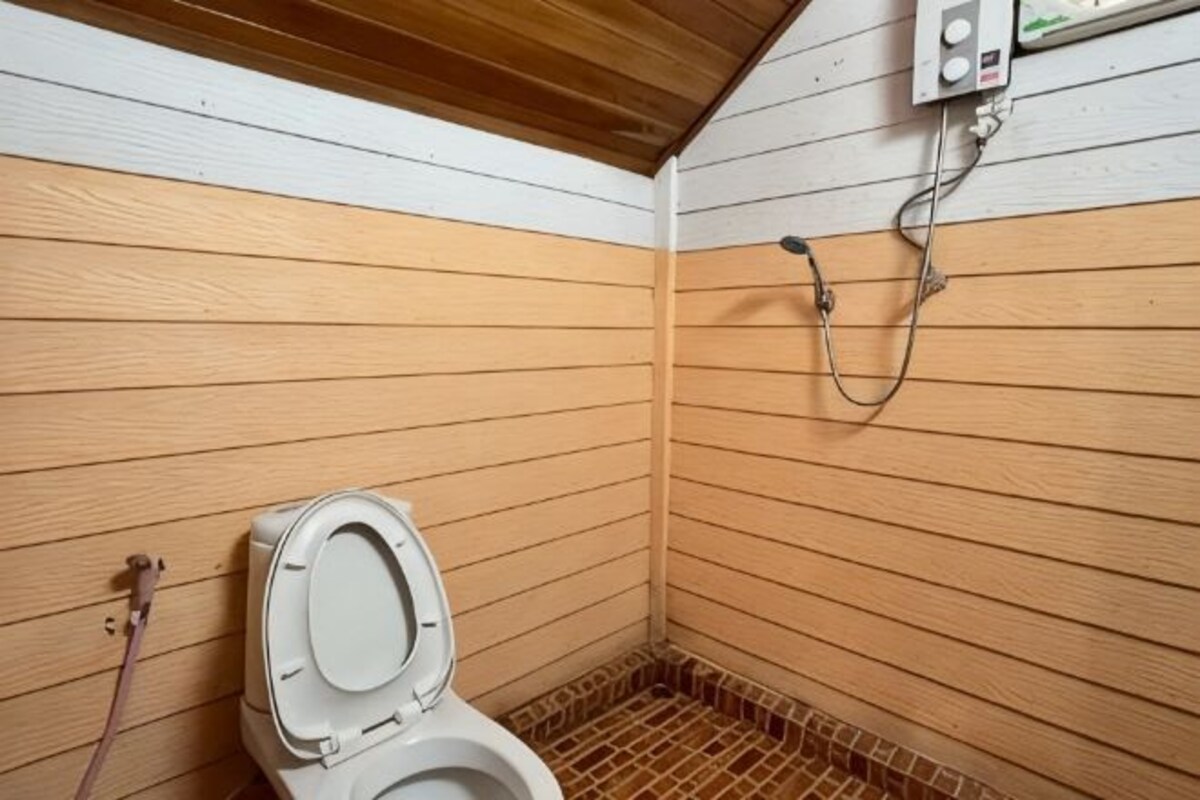 A wooden-paneled bathroom with a toilet, a shower, and a visible electrical outlet.