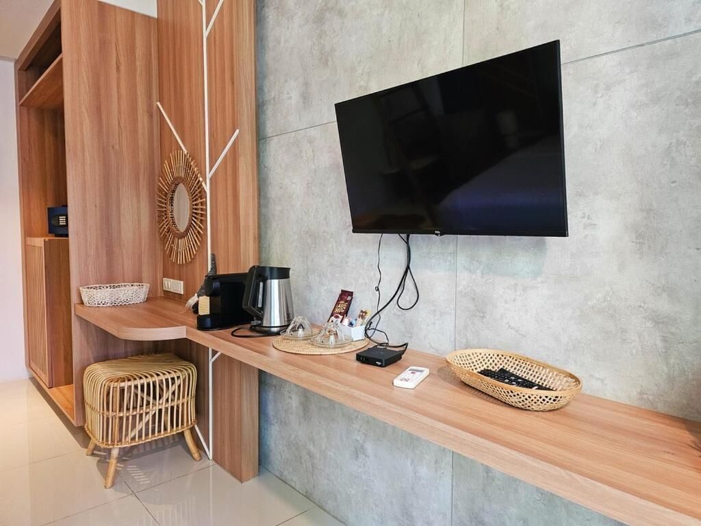 Un espace d’accueil moderne, avec un comptoir en bois, un téléviseur à écran plat fixé au mur et un petit coin salon agrémenté d’un tabouret en osier.