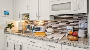 A modern kitchen with white cabinets, a granite countertop, a microwave, a kettle, a toaster, and a blender.