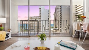 A modern hotel room with a balcony, a dining area, and a view of the cityscape.